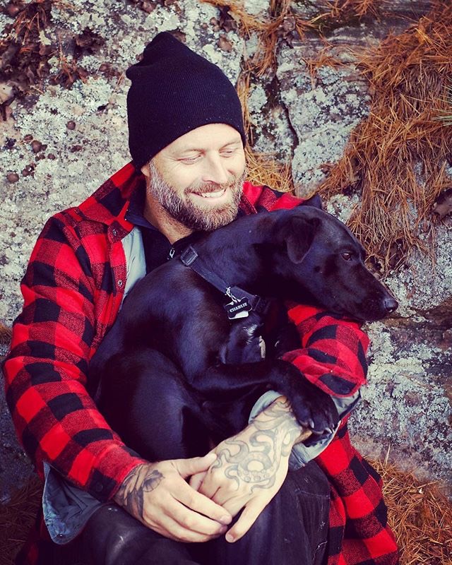 Mark sitting against a rock, holding Charlie, a black dog