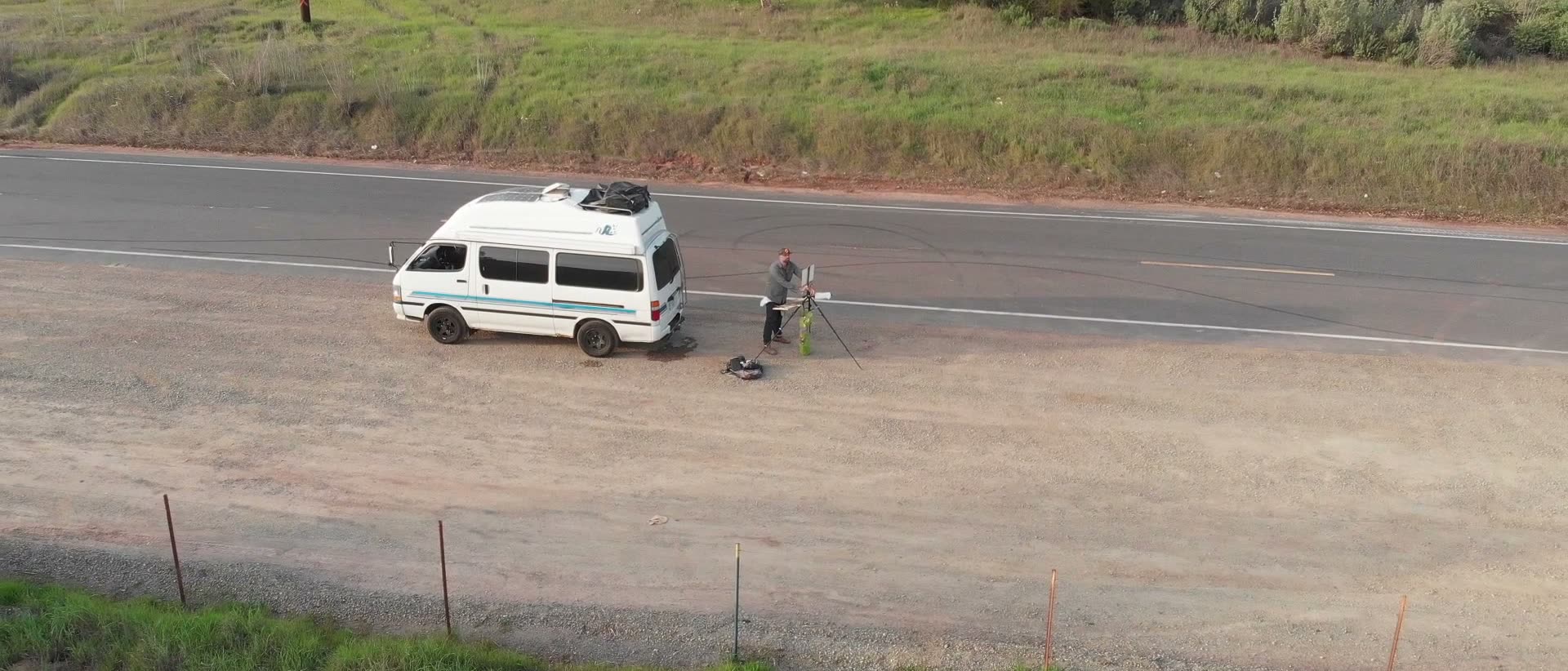 From the air: the van parked on the shoulder of a country road, Mark at his easel beside it