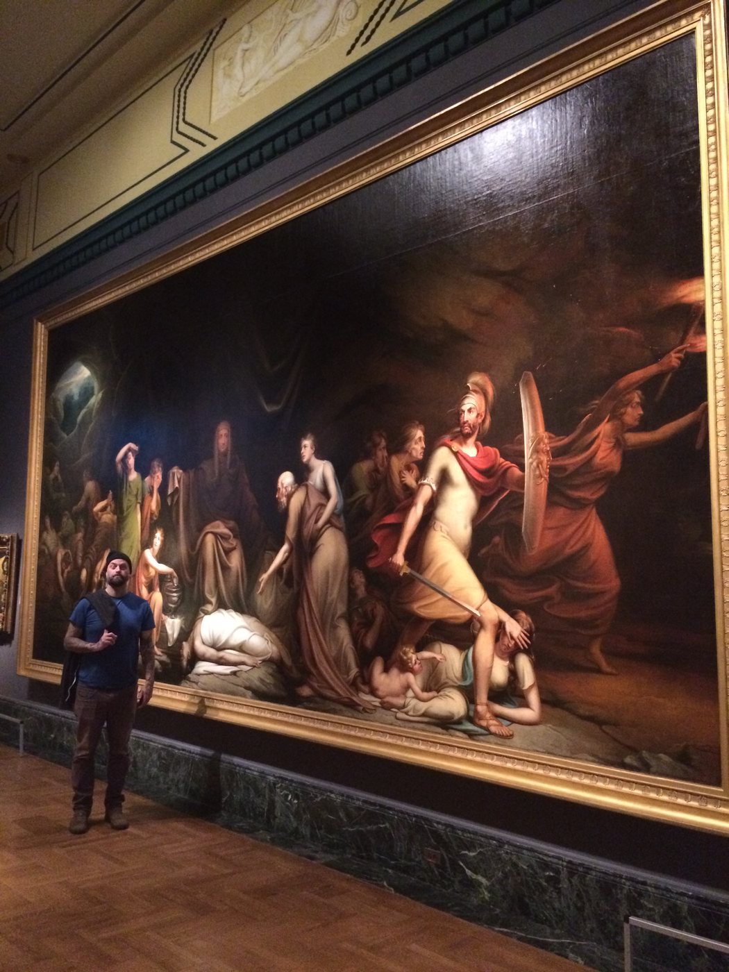 Mark standing beside a huge figure painting in a museum