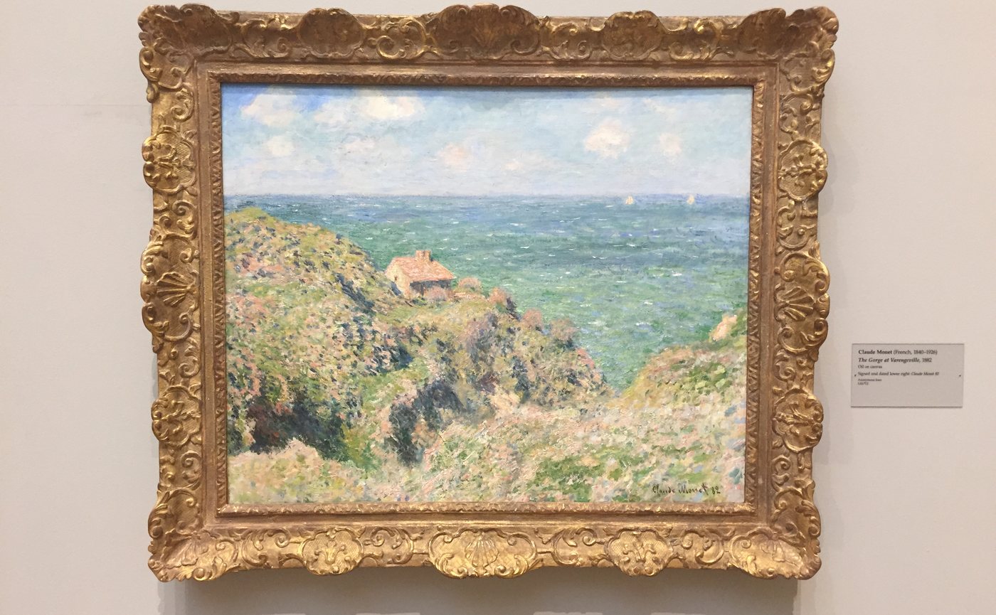 A painting of a green clifftop above the sea in a gold frame