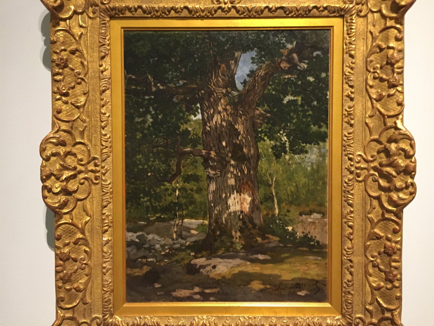 A dark painting of a great oak tree in a gold frame