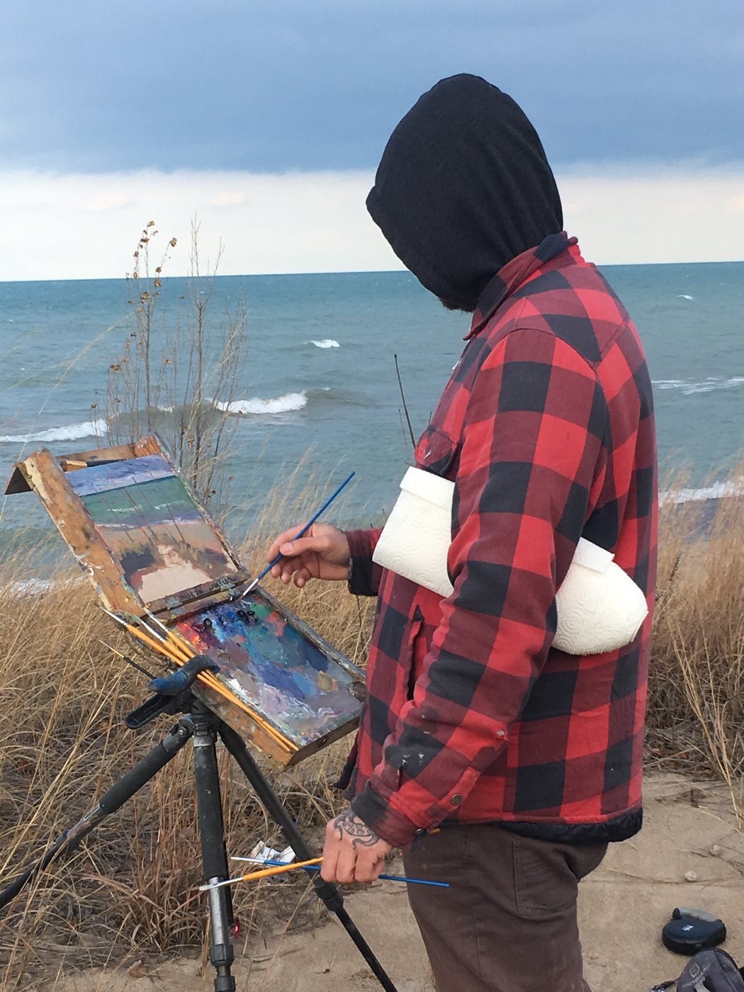 Mark in a red plaid jacket painting at his easel on the dunes above Lake Huron