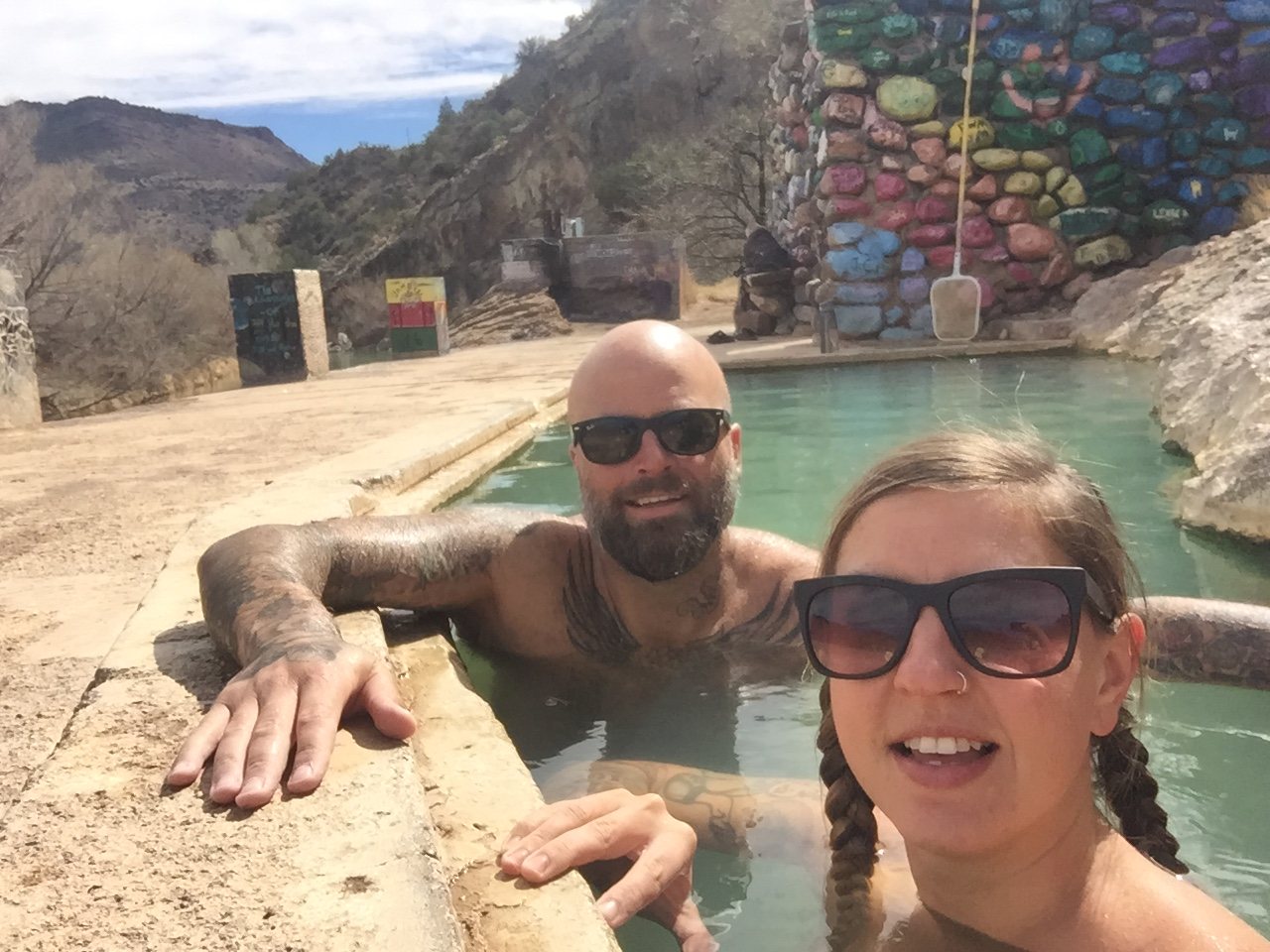 Mark and Jayna in a warm green pool at Verde Hot Springs, painted rocks behind