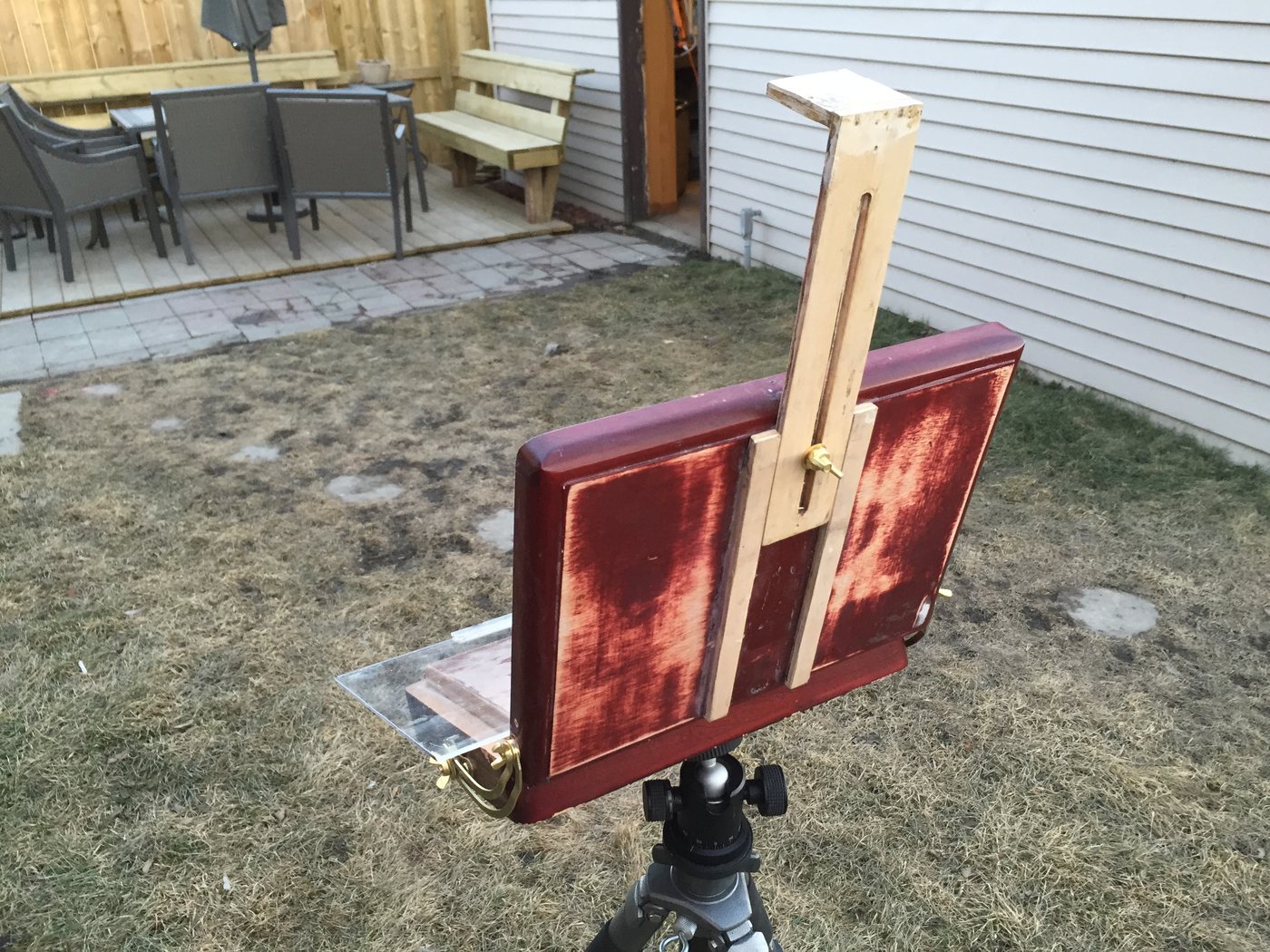 The red cigar-box easel with its sliding wooden top, on a tripod in a back yard