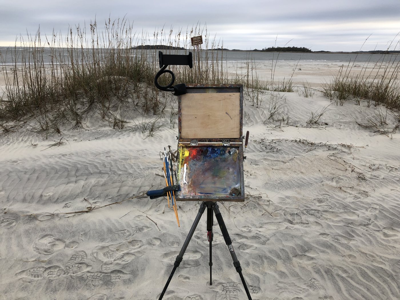 The pochade box on a tripod on a sand dune, panel in the lid, palette below, brushes in the side holder