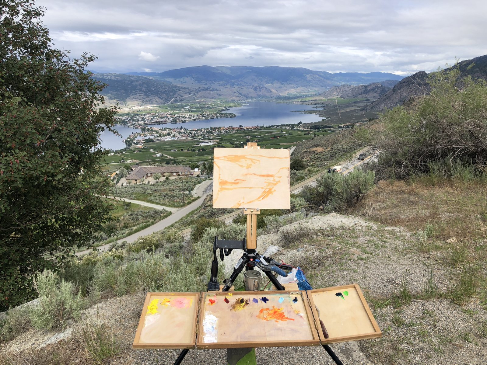The fold-out easel on a hillside above Osoyoos Lake, wings open, an orange-toned panel on the mast