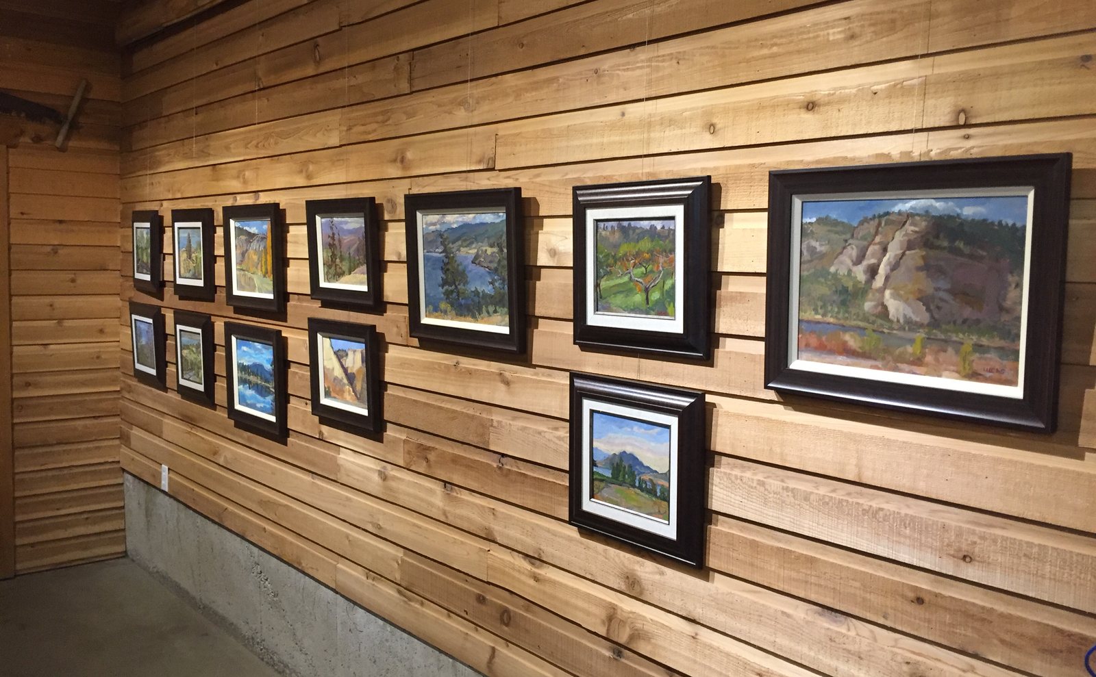 A wall of framed paintings, large and small, on cedar boards