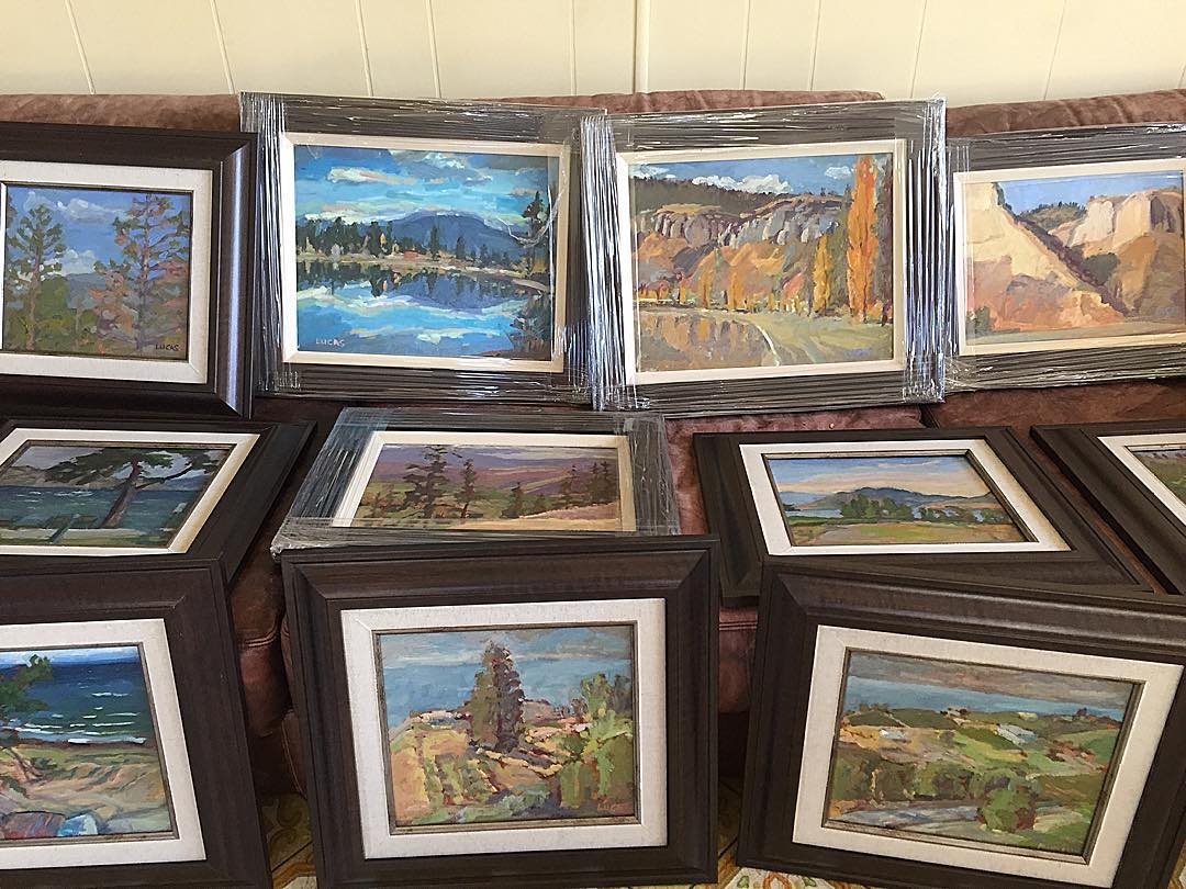 Framed paintings wrapped in plastic, laid out on a sofa before a show