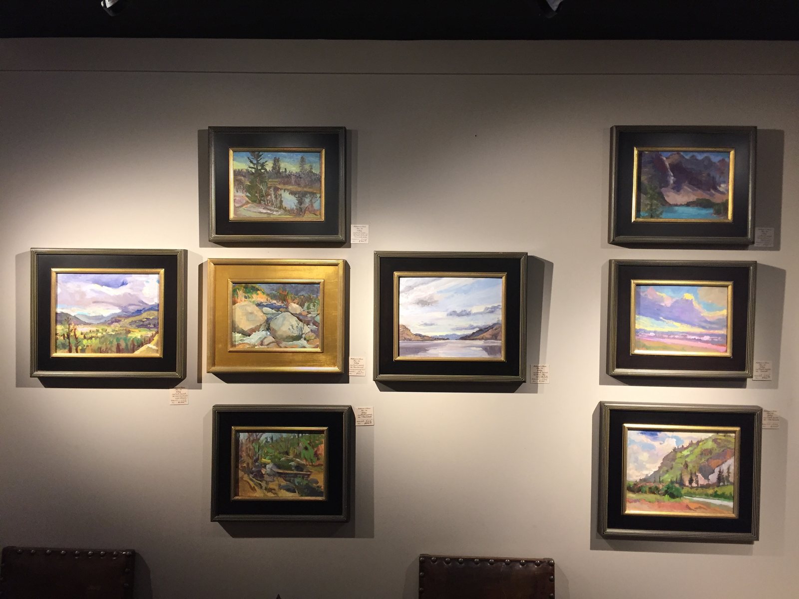 Eight framed paintings lit on a grey gallery wall
