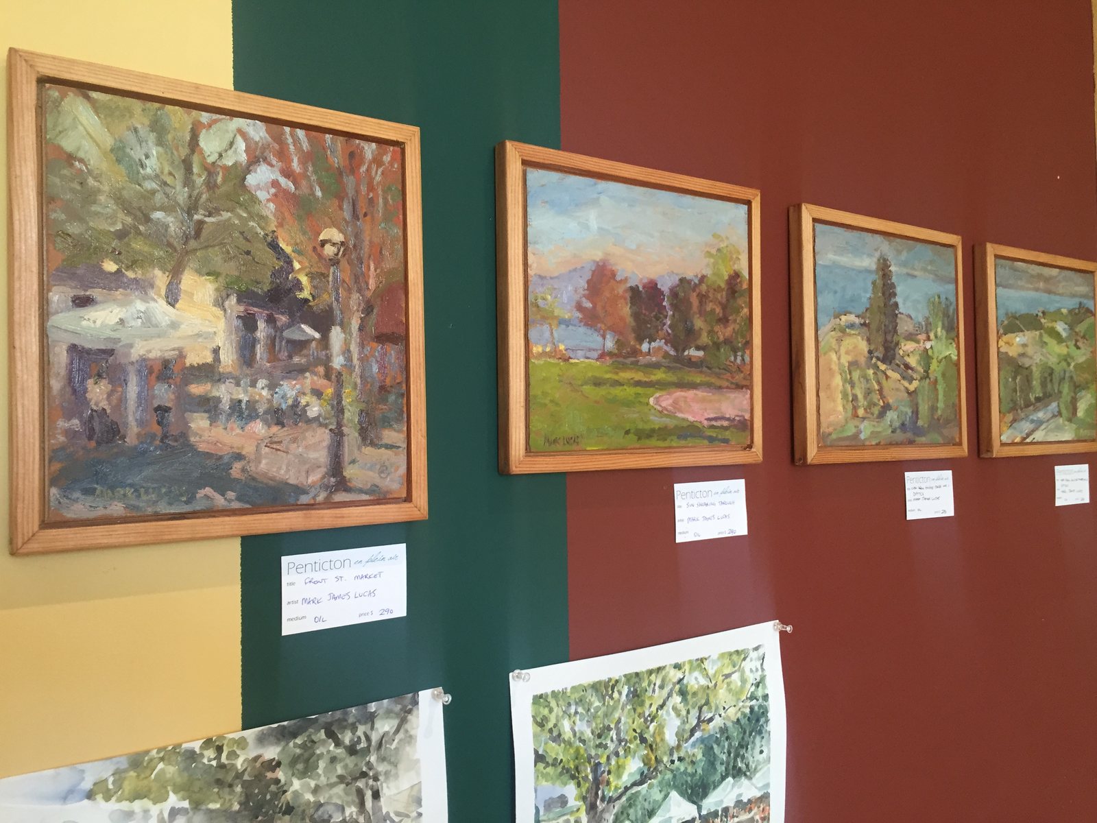 Framed early paintings on green and red gallery walls with labels