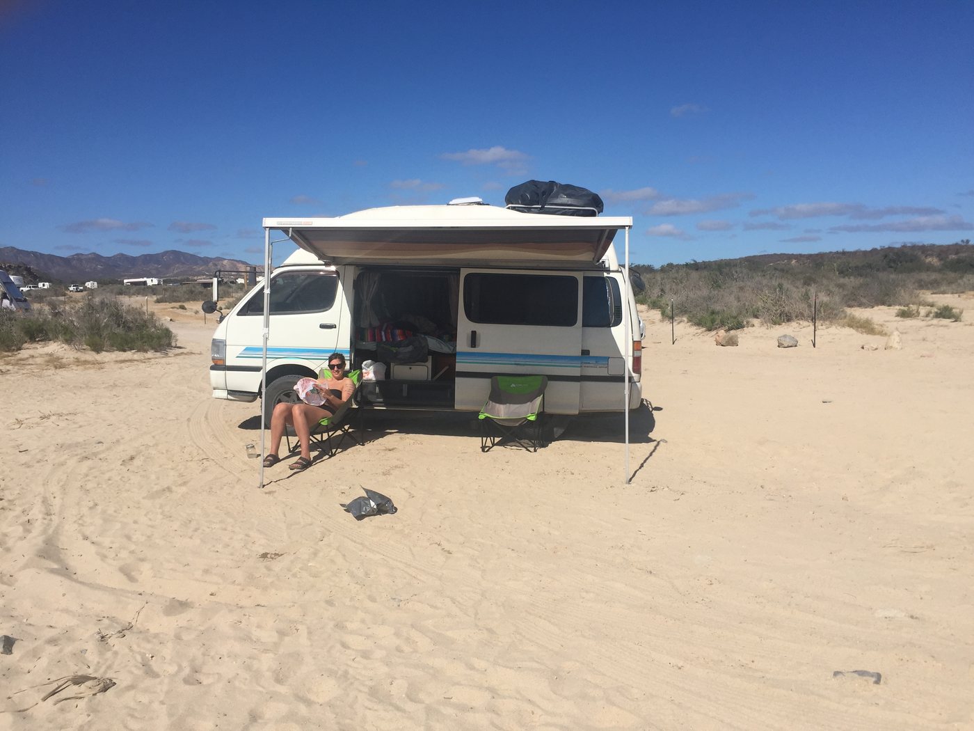 The van on the sand with its awning out, a chair in the shade